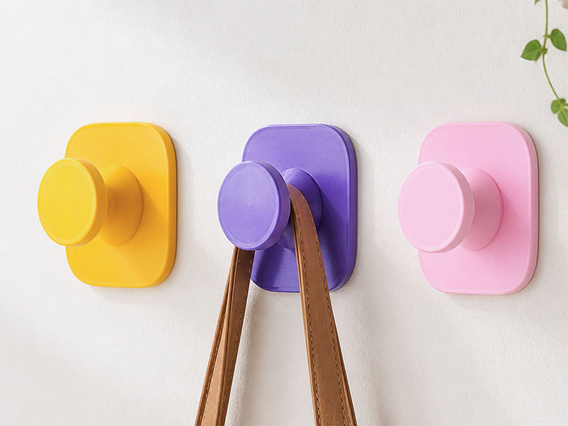 Colorful PETG 3D printed wall hooks in yellow, purple, and pink